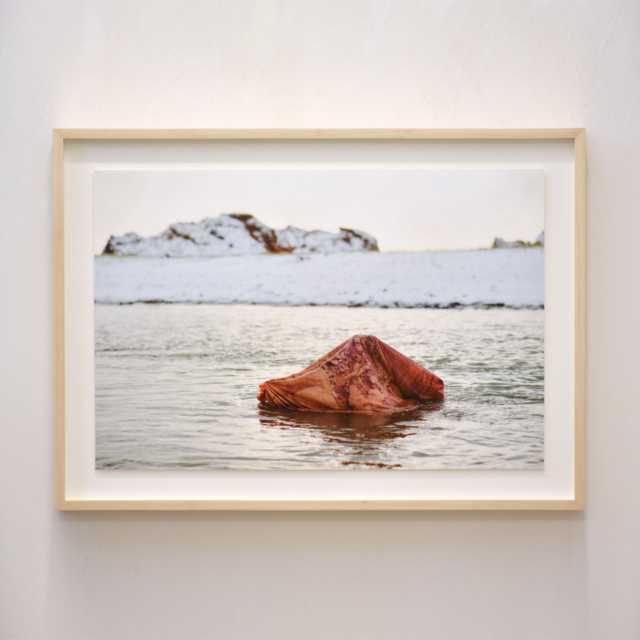Arpenter l’archipel, par Alphiya Joncas. Photographie hivernale. Une personne se trouve sous un drap, immergée sous l’eau glacée. Îles de la Madeleine.