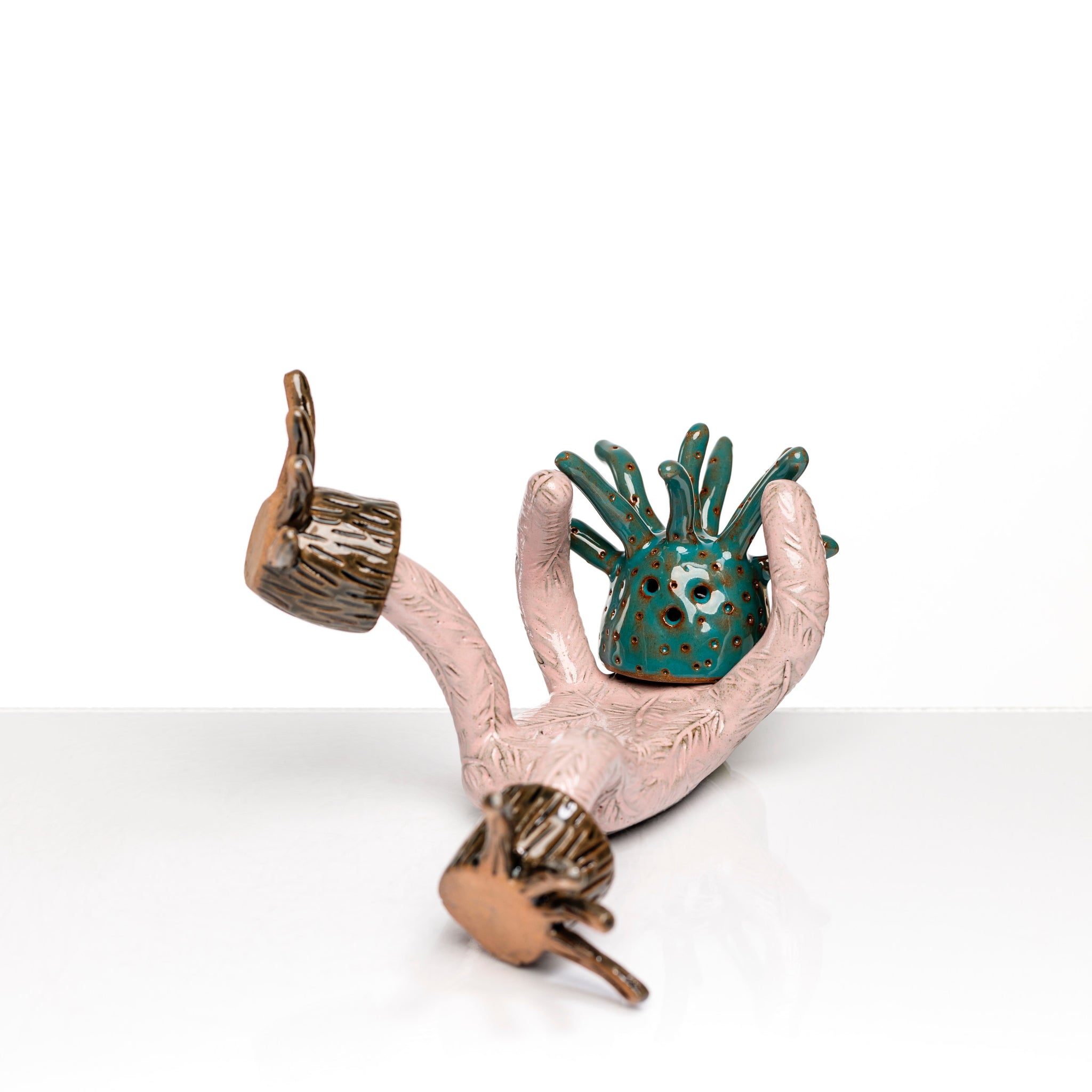 Sculpture en céramique par Fanny Mesnard. Un personnage rose avec une tête de pieuvre et des pieds en bois est en perte d’équilibre sur le dos.