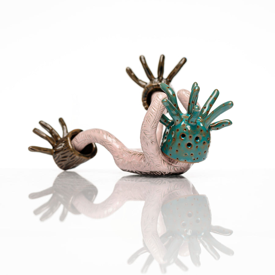 Sculpture en céramique par Fanny Mesnard. Un personnage rose avec une tête de pieuvre et des pieds en bois est en perte d’équilibre sur le dos.