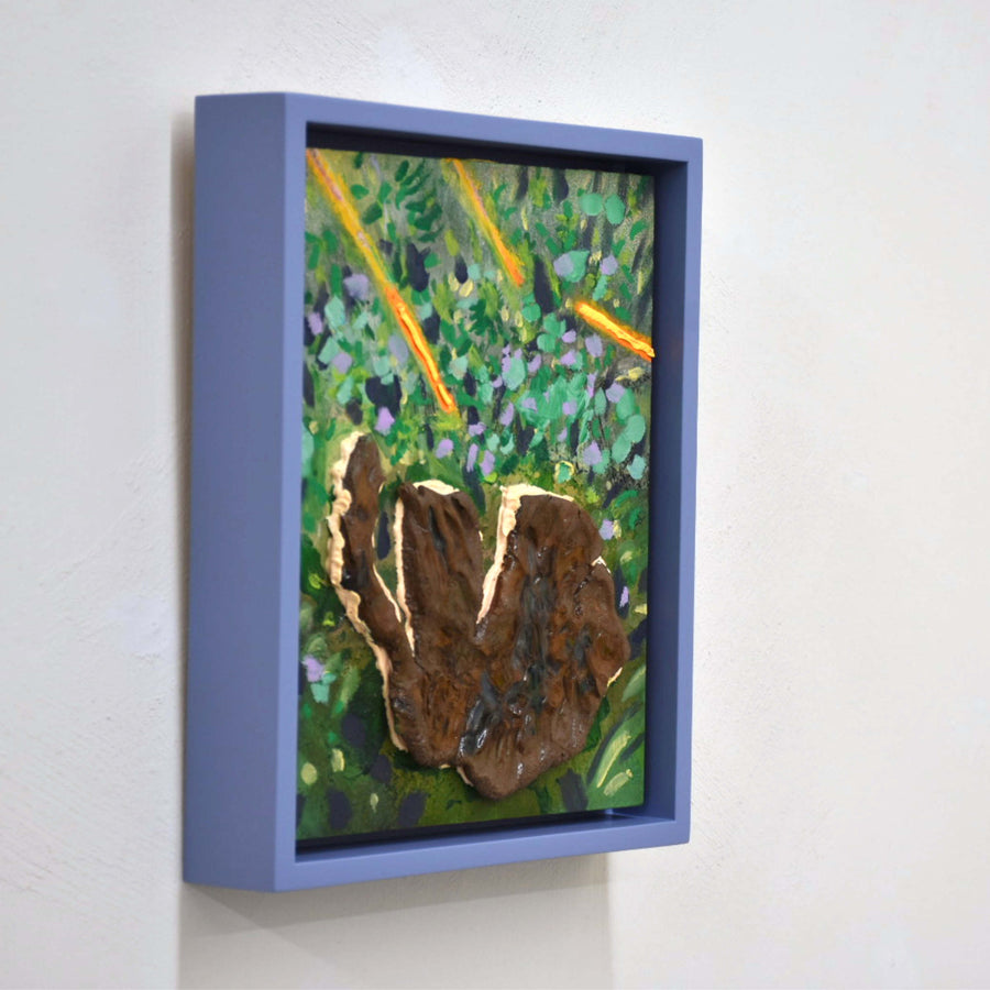 Branches fluos, de Josiane Lanthier. Acrylique et céramique sur panneau de bois, 8” x 10” avec cadre violet. Branches oranges fluos dans du gazon vert avec une grosse pierre brune.