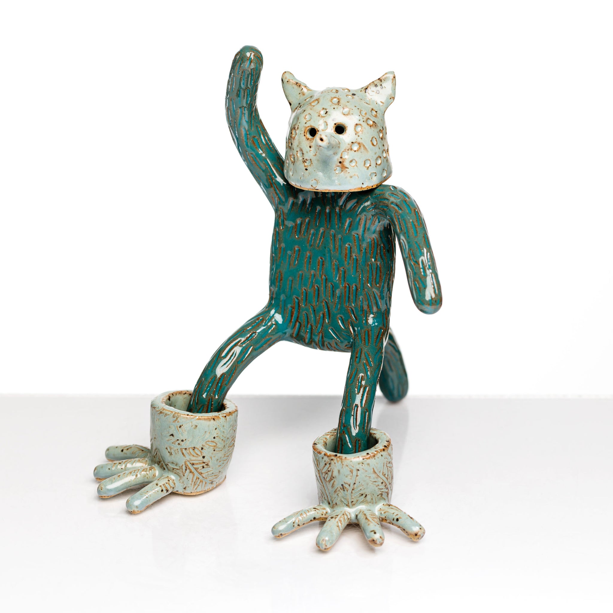 Sculpture en céramique par Fanny Mesnard. Un personnage avec une tête de chien et des pieds de grenouille se tient debout en équilibre sur sa queue.