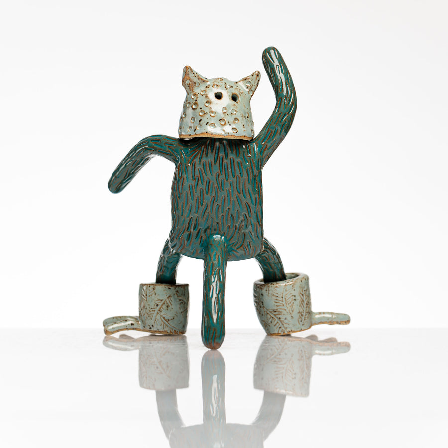 Sculpture en céramique par Fanny Mesnard. Un personnage avec une tête de chien et des pieds de grenouille se tient debout en équilibre sur sa queue.