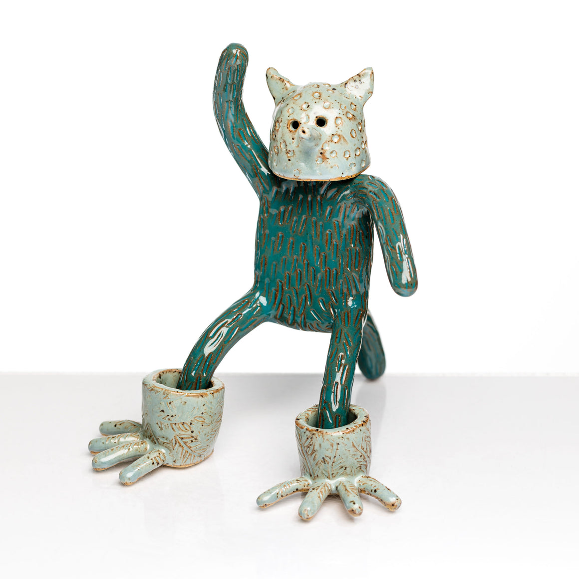 Sculpture en céramique par Fanny Mesnard. Un personnage avec une tête de chien et des pieds de grenouille se tient debout en équilibre sur sa queue.