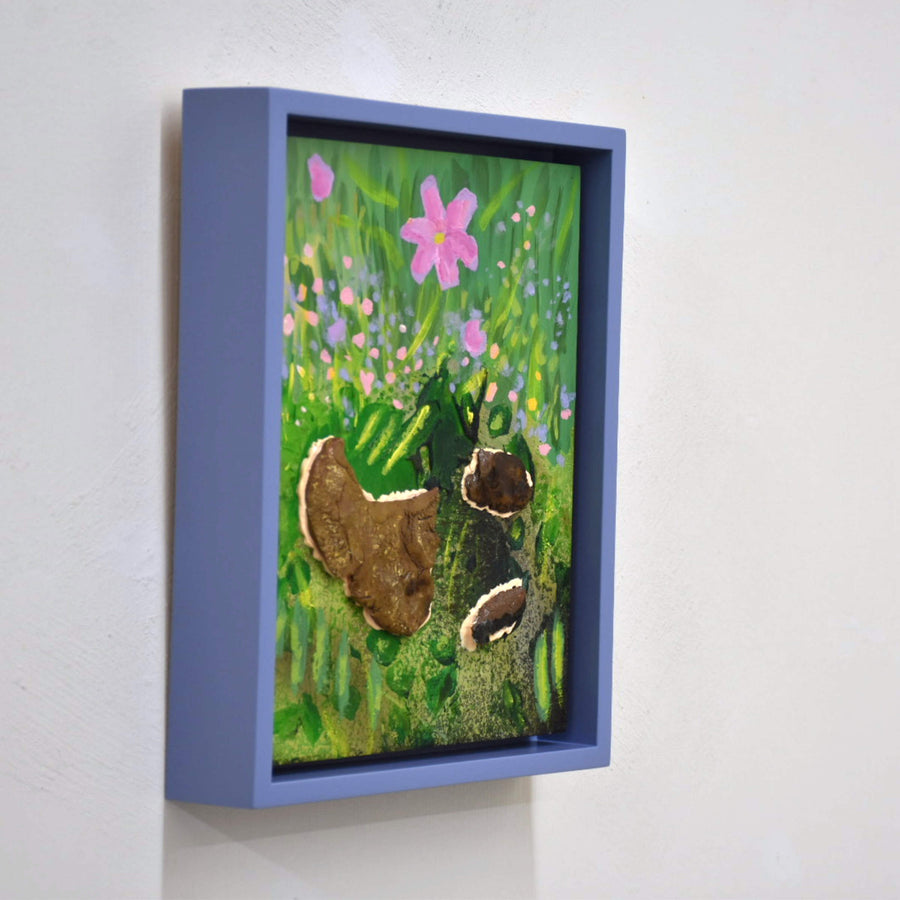 Cosmos, par Josiane Lanthier. Acrylique et céramique sur bois, petit format, cadre violet. Cosmos en fleur rose dans gazon vert avec roches.