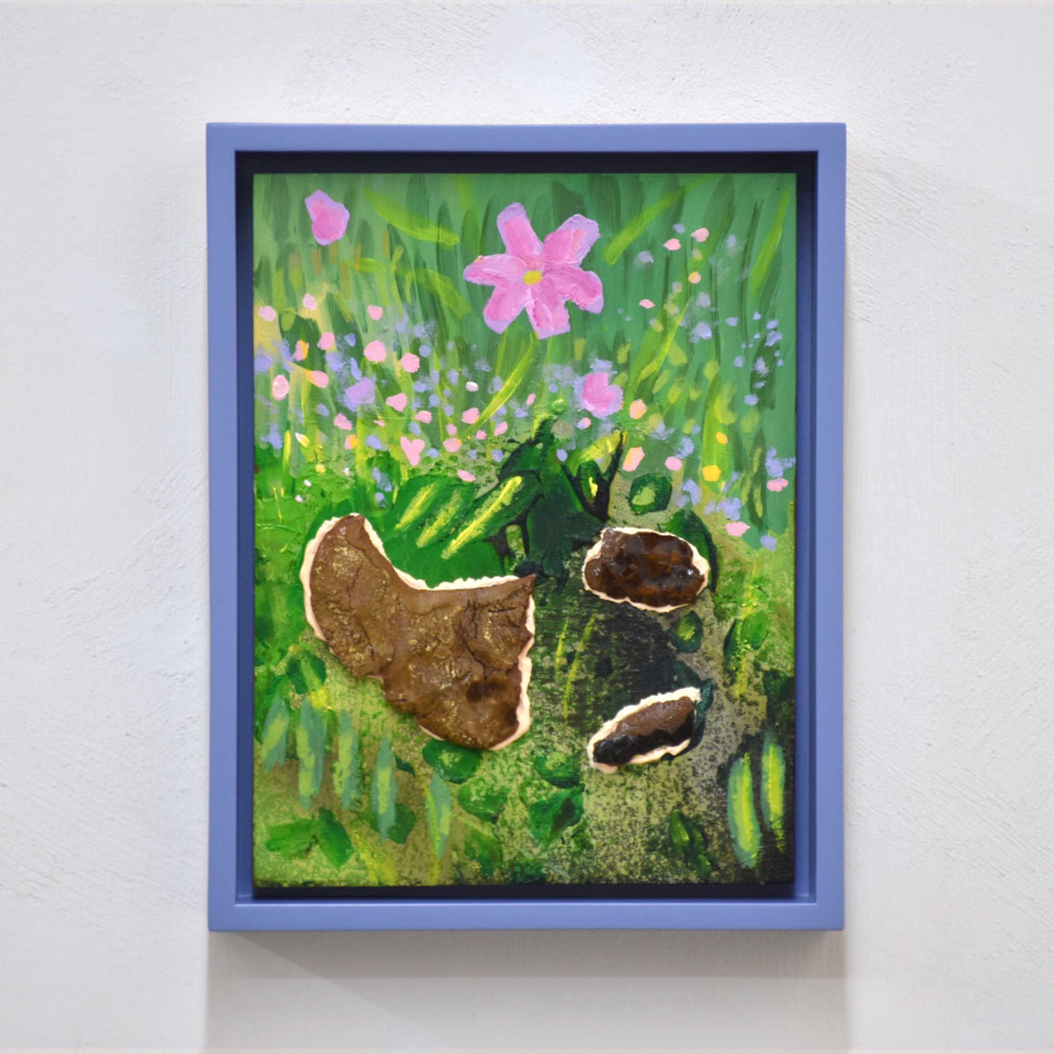 Cosmos, par Josiane Lanthier. Acrylique et céramique sur bois, petit format, cadre violet. Cosmos en fleur rose dans gazon vert avec roches.