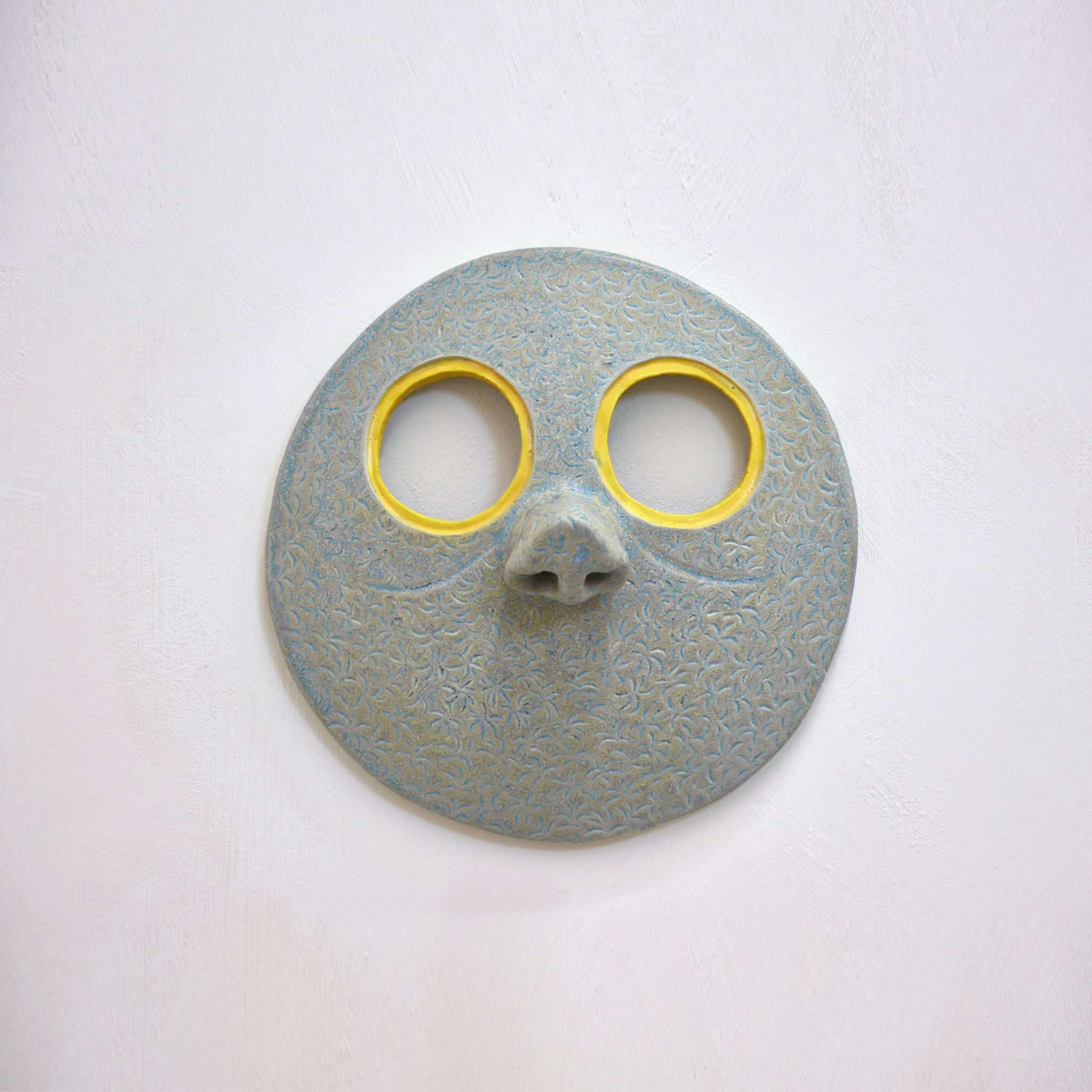 Masque mural en céramique de Fanny Mesnard. Un visage vert au grand nez et aux yeux jaunes.