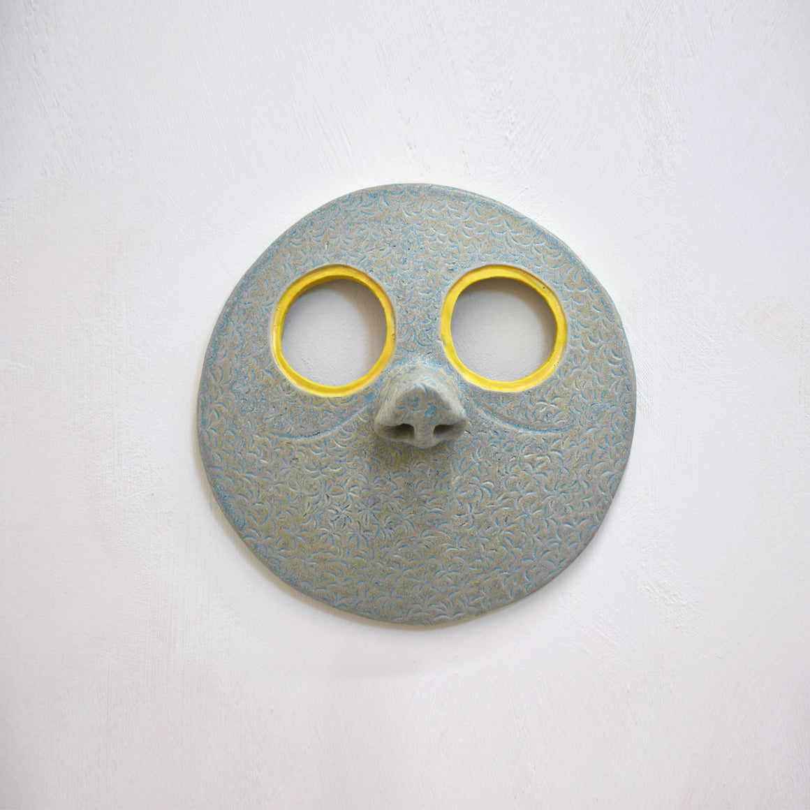 Masque mural en céramique de Fanny Mesnard. Un visage vert au grand nez et aux yeux jaunes.