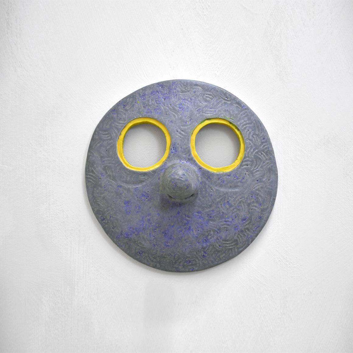 Masque mural en céramique de Fanny Mesnard. Un visage bleu au grand nez et aux yeux jaunes.