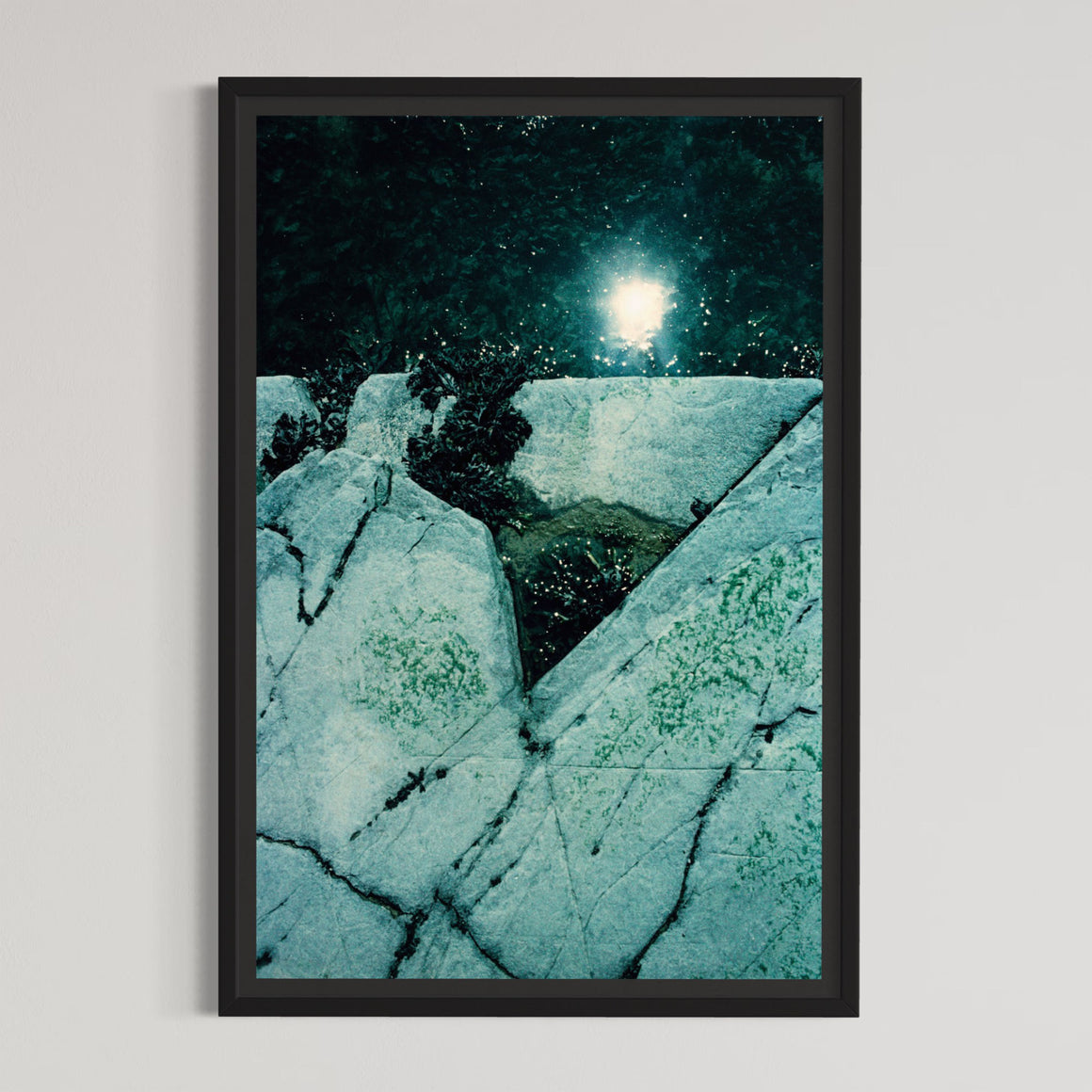 Triangle désamorcé, par Éva-Maude TC. Photographie sur pellicule 35 mm, tirage limité de 4 exemplaires. Nuances de vert et de turquoise, reflet du soleil dans l’eau, rocher de rivage.