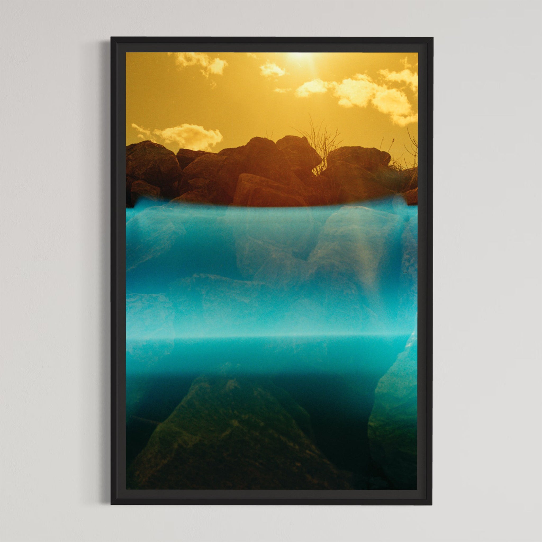 Zone intertidale, par Éva-Maude TC. Photographie contemporaine sur pellicule 35 mm, 24” x 36”, tirage limité de 4. Encadrement noir. Ciel jaune sur fleuve de lumière bleue, rochers de rivage.