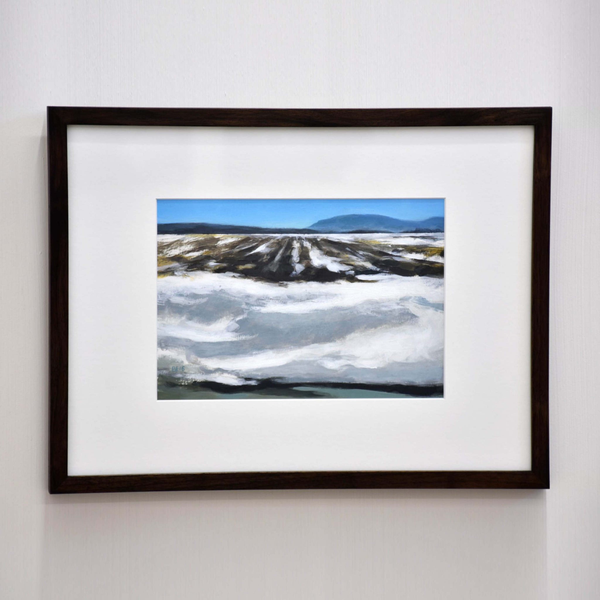 Champ de mars, de Benoit Chartier. Acrylique sur papier Bristol, 13” x 17” avec cadre en noyer, 2016. Composition d’un champ partiellement couvert de neige. Ciel bleu à l’horizon.
