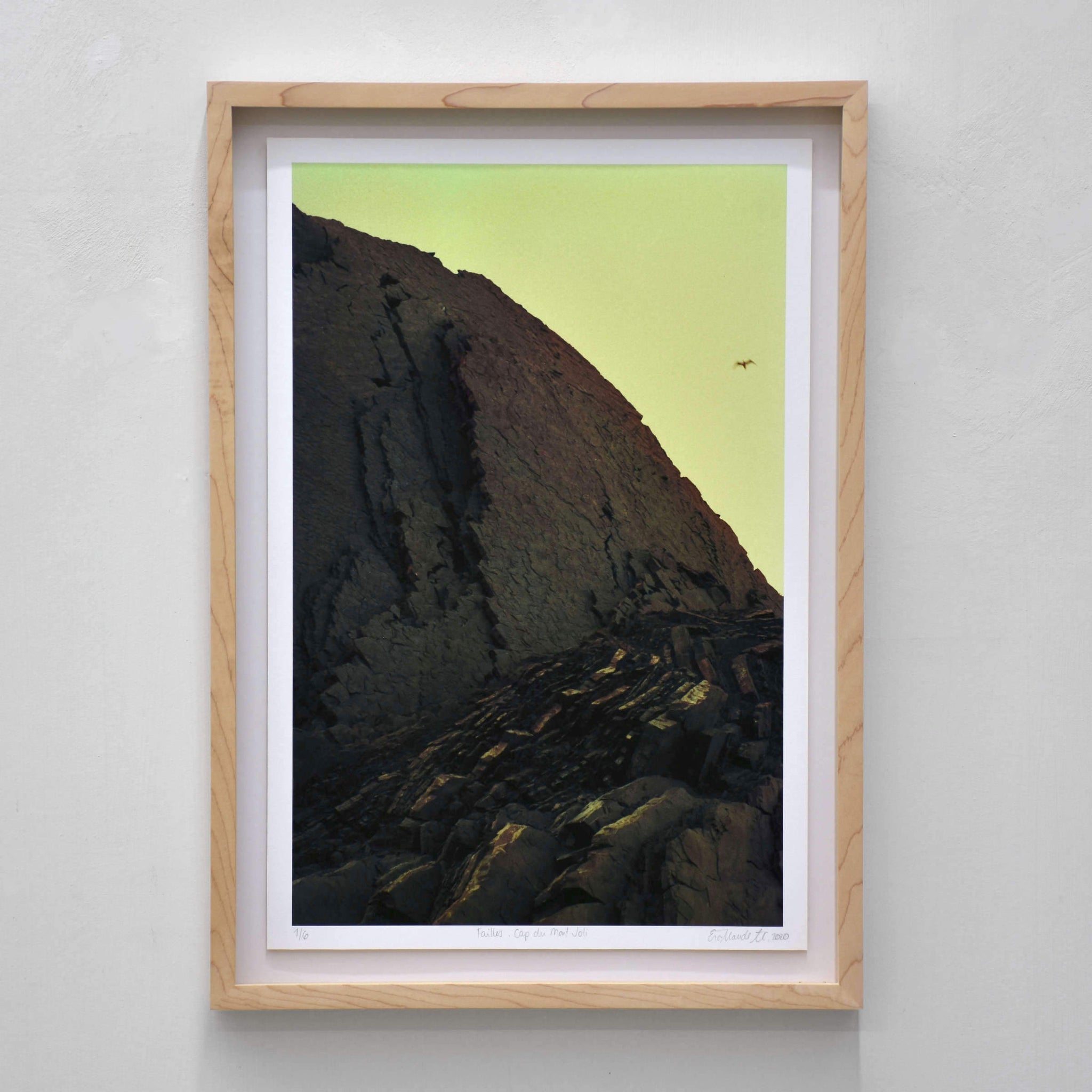 Failles, Cap du Mont-Joli, par Éva-Maude TC. Photographie contemporaine sur pellicule 35 mm. Une falaise d’ardoise dans un ciel vert survolée par un oiseau.