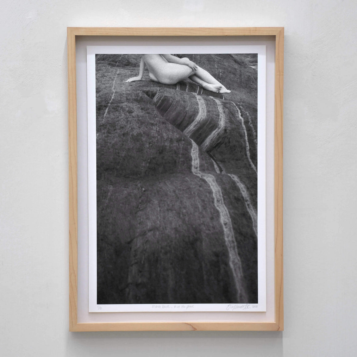 Marée basse, rue du Phare, par Éva-Maude TC. Photographie en noir et blanc d’un modèle vivant nue sur des rochers d’ardoise, sur le bord du fleuve.