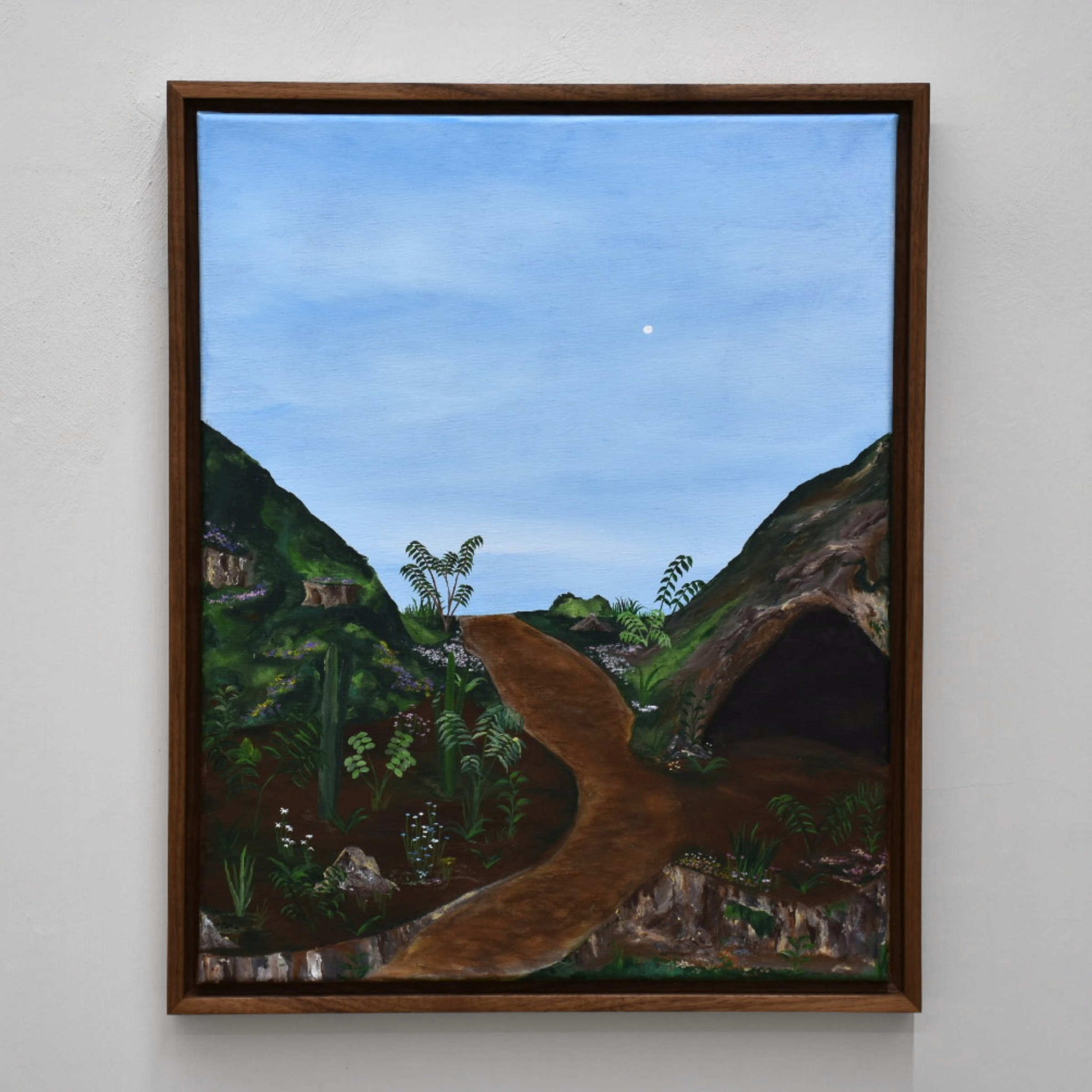 Sans titre, de Gabriel Rioux. Acrylique sur toile, 16” x 20”, cadre en noyer, 2022. Peinture de paysage, genre naïf, ciel bleu pâle et grotte sur colline verte.
